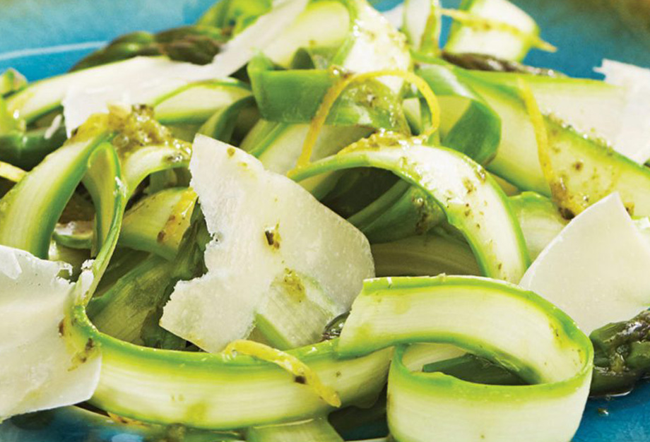 Ribbons of green, raw asparagus served as a salad with a lemon-pesto dressing on top of a blue plate.