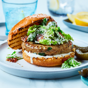 Turkey Kale Burger topped with Caesar salad dressing on a sesame seed bun with quick pickles and Parmesan cheese.