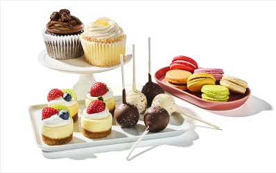 An assortment of dessert trays holding cupcakes, mini cheesecakes, cake pops, and macrons. 
