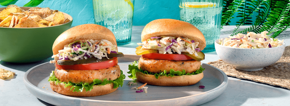 Two spicy dill pickle salmon burgers with bowl of coleslaw to the side