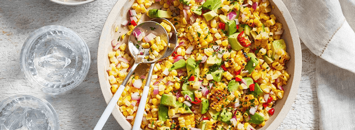 <p>Corn and avocado salad in large cream serving bowl with serving tongs</p>