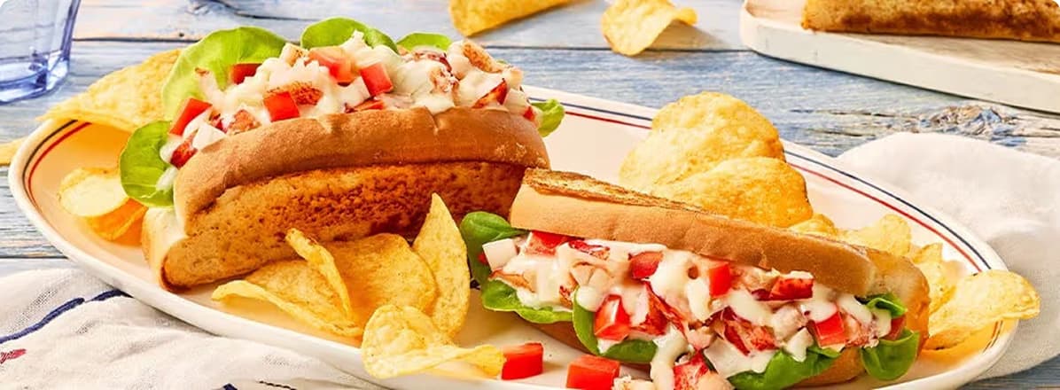 Two lobster rolls on a plate topped with Donair sauce with a side of chips