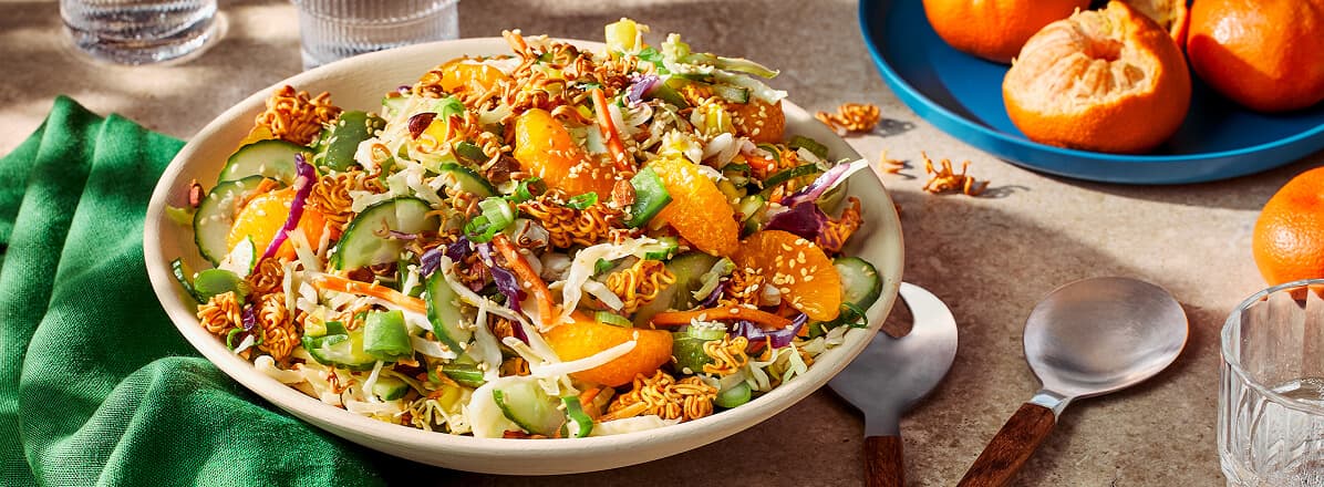 Asian ramen salad in a white bowl with mandarins in the background