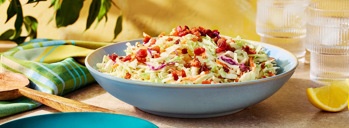 Caesar Salad Inspired Slaw in a white bowl topped with bacon bits