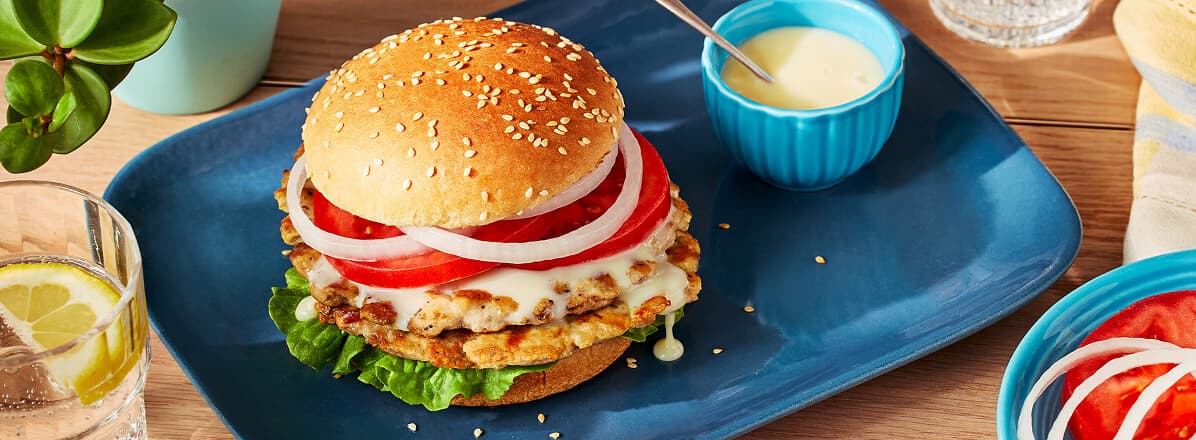 Chicken smashed burger on bun topped with Donair sauce, sliced tomato and onion.
