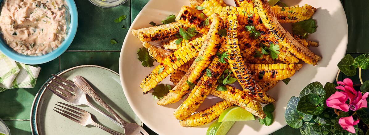 Overhead shot of corn ribs on a white plate, corn ribs have been charred and topped with spices, and cilantro