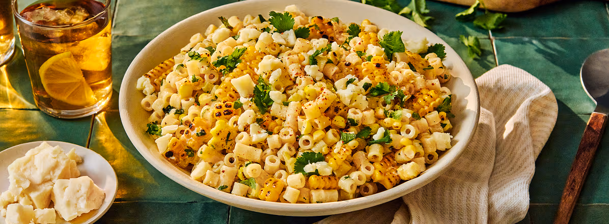 Shot of white bowl with Mexican-inspired corn pasta salad with ditali pasta and topped with cilantro and feta cheese