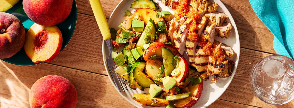 Overhead shot of grilled chicken thighs with kimchi, peach, and cucumber salad.