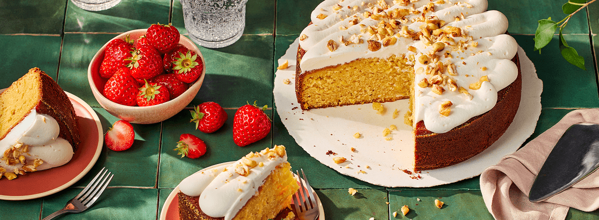 Sweet corn cake with one slice taken out and on a plate, topped with whipped cream and sweet corn crumb