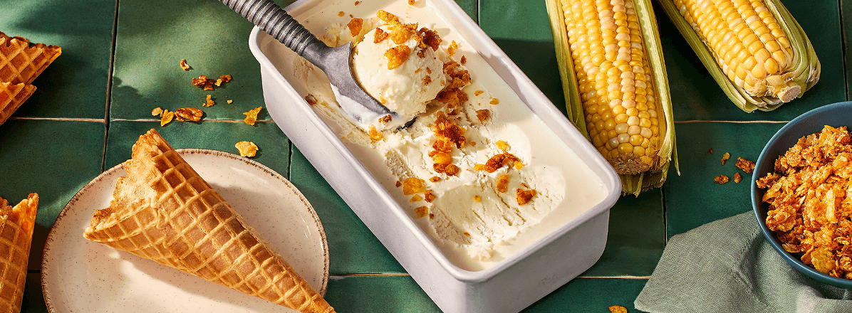 Sweet corn ice cream in tub with scoop of ice cream taken out and a waffle cone to the side