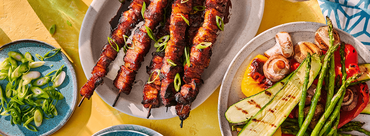 Overhead shot of pork belly skewers with a side of grilled veggies and sliced green onions