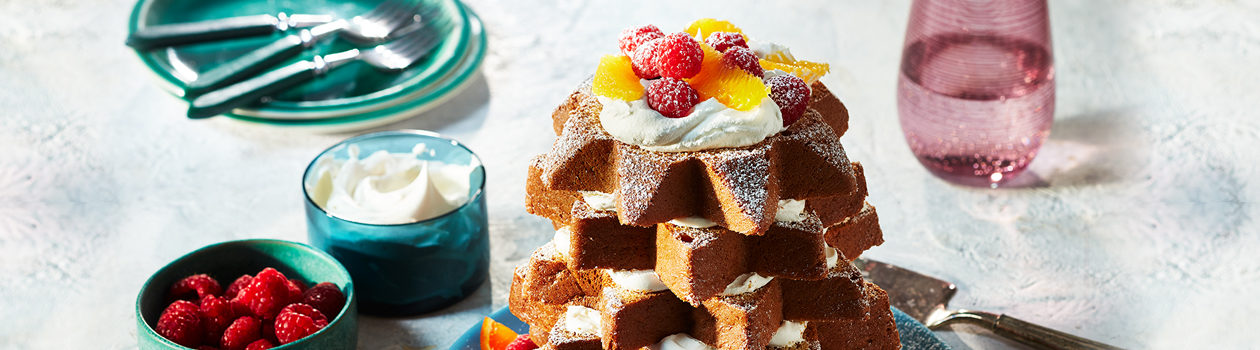 Stacked slices of panettone with icing sugar, cream and fruit on blue serving platter.