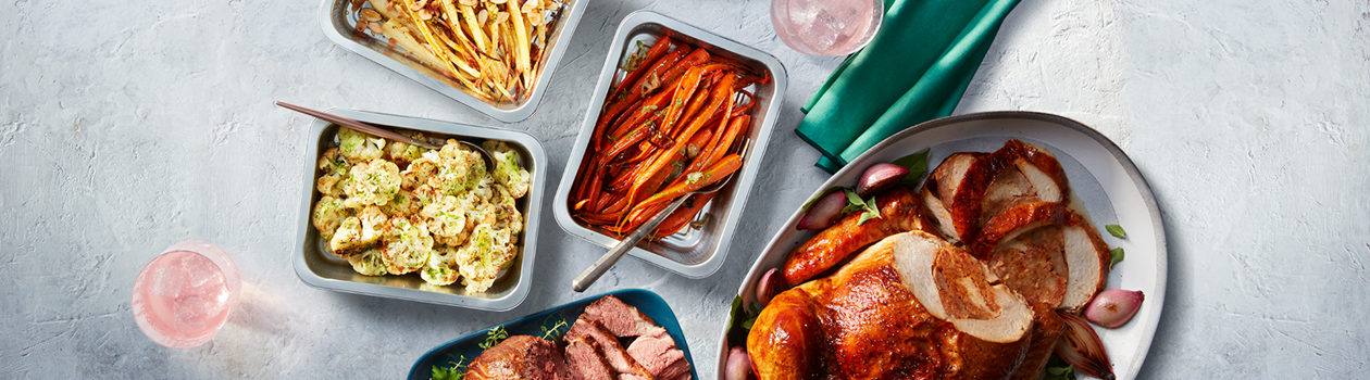 Several cooked roasts on platters ready to serve with a few side dishes around them.