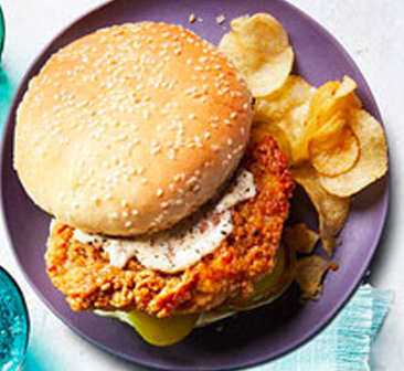 Sliced chicken sandwich on purple plates with side of potato chips.