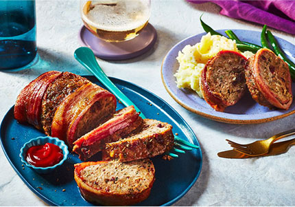 Sliced meatloaf on blue serving platter, with plate of meatloaf, mashed potatoes and green beans to the side