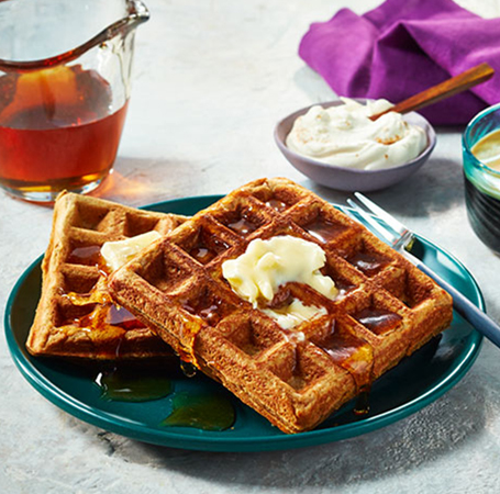 Gingerbread-spiced waffles on aqua-green plate with maple syrup poured over.