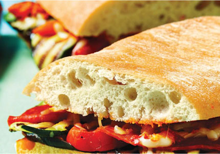 Ciabatta bun stuffed with grilled veggies and sliced in half.
