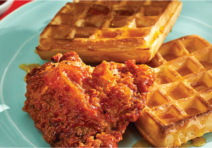 Maple-glazed fried chicken piece sitting next to golden waffles on plate.