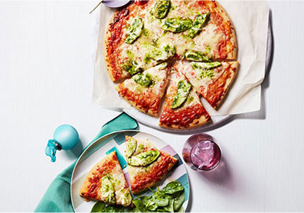 Pesto pizza sliced and on marble plate.