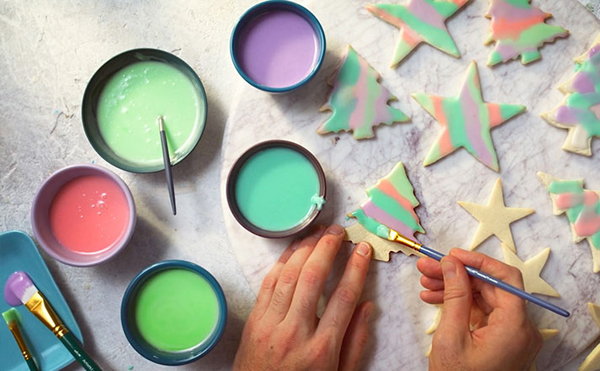 hands painting sugar cookies with thin royal icing in various colours