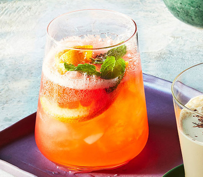 Stemless wineglass filled with blood orange spritz non-alcoholic cocktail, ice, an orange slice and fresh infarm mint.