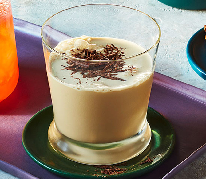 Short decorative clear glass filled with milky coffee-coloured non-alcoholic cocktail, topped with fresh nutmeg.