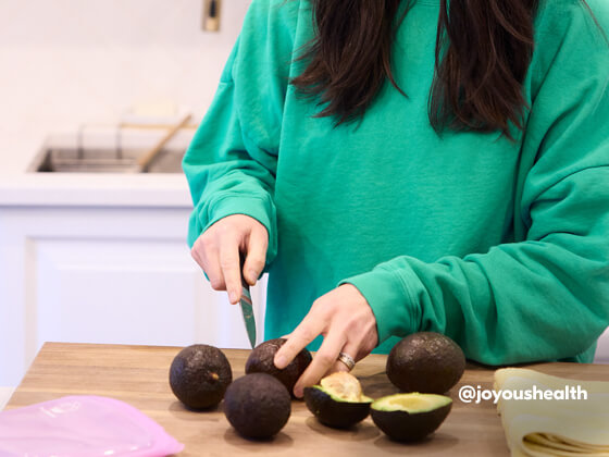 Joy stands at kitchen counter cutting avocados in half