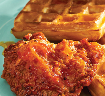 Maple-glazed fried chicken piece sitting next to golden waffles on plate.