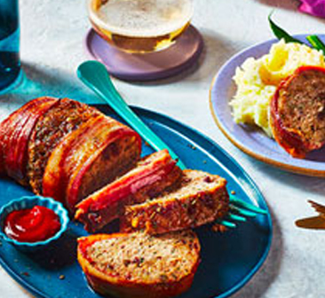 Sliced meatloaf on blue serving platter, with plate of meatloaf, mashed potatoes and green beans to the side