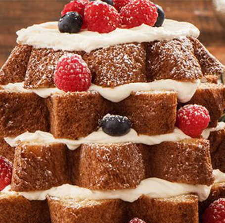 Stacked slices of panettone with icing sugar, cream and fruit on blue serving platter.