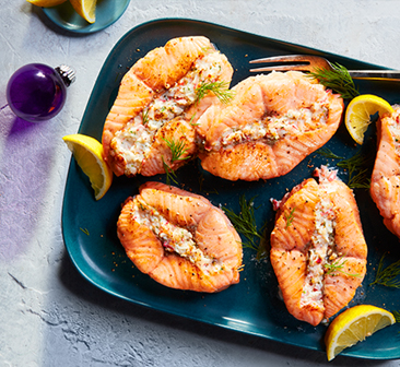 Roasted salmon slices stuffed with cheddar and spinach, cold-water shrimp, bacon, and herbs on a blue platter with lemon wedges.