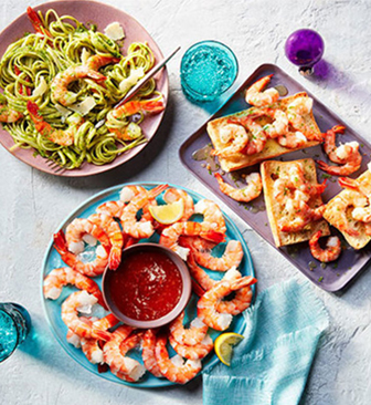 Shrimp ring on blue plate with cocktail sauce and shrimp on pasta, and on toast on two other plates.