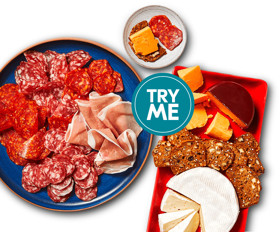 try-me-charcuterie-mega-deal One platter of cheese and crackers with fruit, and the other holds thin slices of cured meats.
