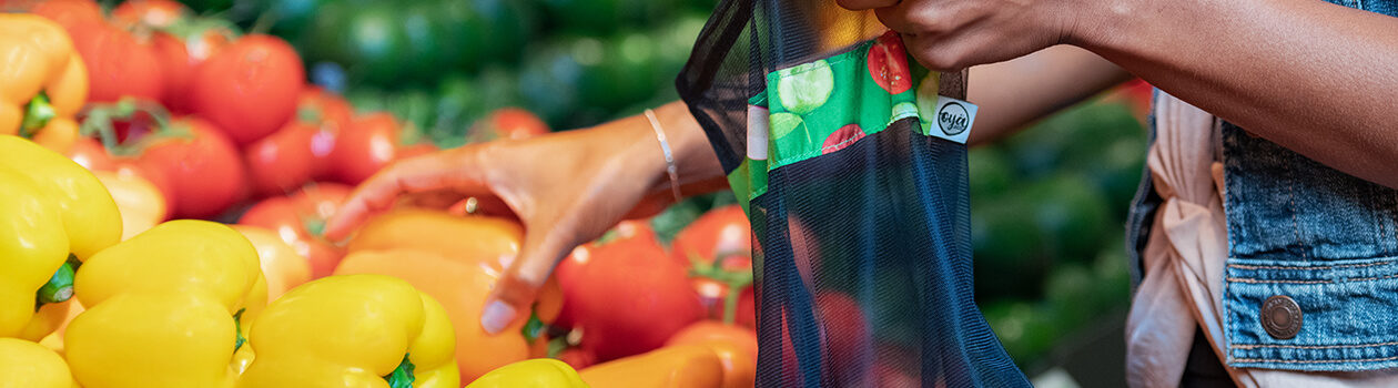 Person picking out orange bell peppers from the produce deparment and putting them in mesh reusable produce bag