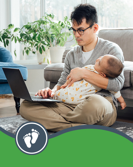Parent holding baby while typing on a laptop