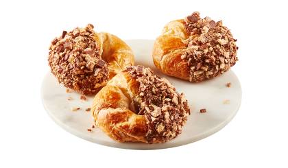 Close up of croissant half dipped in Coffee Crisp spread that’s coated in candy bar crumbs on white plate.