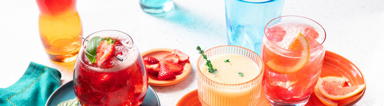 Tumbler glass filled with a slushy-type beverage made of citrus sorbet, citrus soda and tonic water on an orange platter.