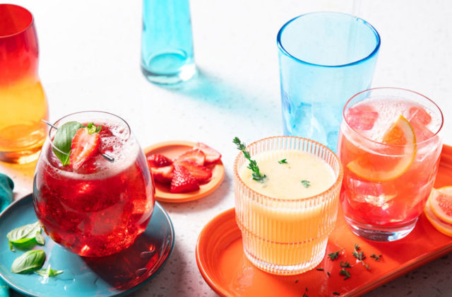 Tumbler glass filled with a slushy-type beverage made of citrus sorbet, citrus soda and tonic water on an orange platter.