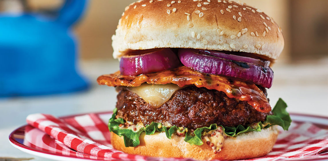 burger on a red and white napkin with red onion, cheese, lettuce