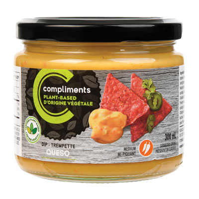 A clear glass jar of Compliments Plant-Based Queso Dip pictured as a dip alongside red tortilla chips on the jar artwork.