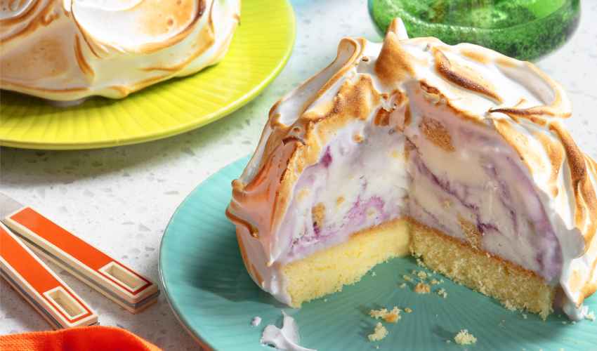 Fire-Ice-BlueberryBaked-alaska Two individual-sized baked Alaskas on separate blue and yellow plates with bruleed tops, next to an orange napkin and two glasses of water.