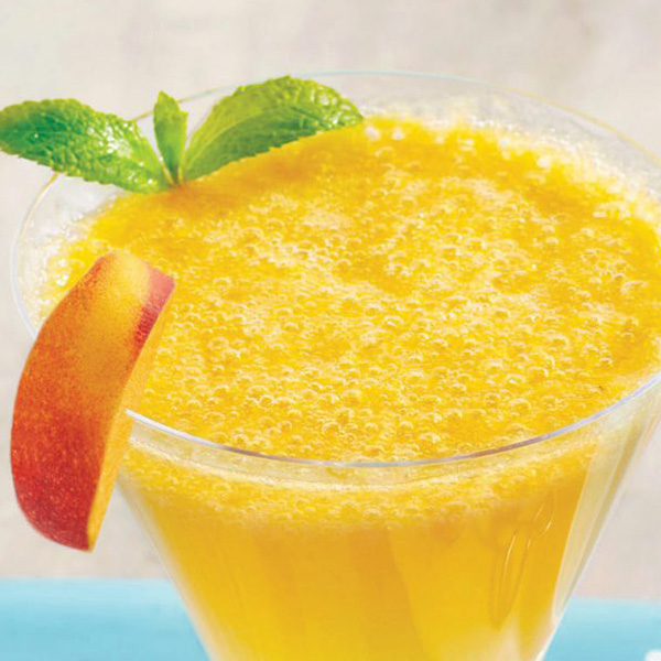 Close-up of a glass filled with a yellow-gold Bellini made with fresh peaches, lime zest, and ginger ale.