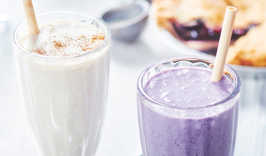 Fruit-pie-shake Two, tall milkshake glasses filled with a fruit pie and ice cream combination, one of which is purple, and in the background you see a berry pie.