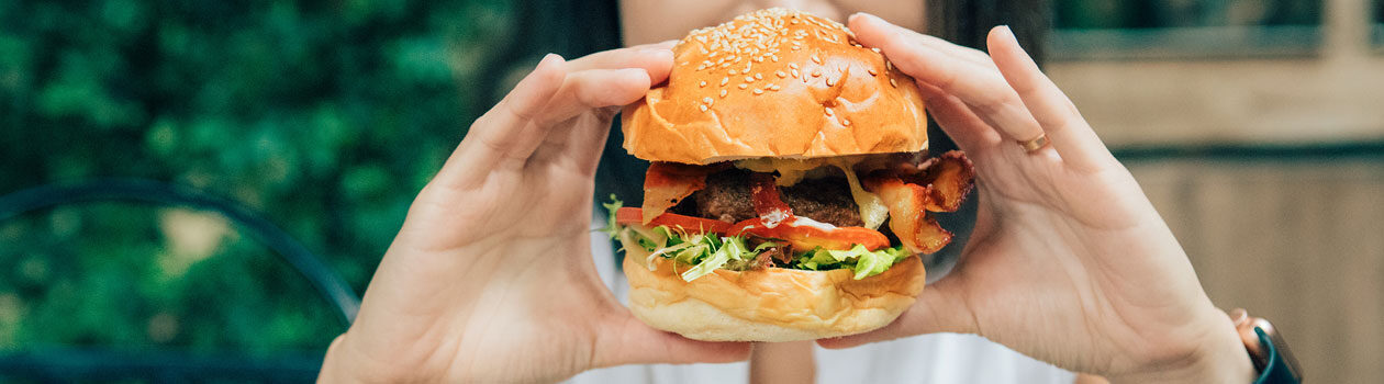 Woman holding a stacked, grilled burger in front of her face, about to take a bite as she sits in her backyard.