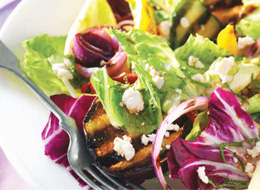 Chopped and grilled zucchini, eggplant, red onion, and red pepper mixed with salad greens, fresh mint, and feta served on a white plate. 