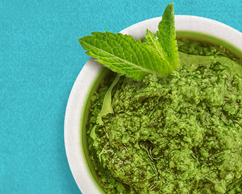 White bowl filled with mint pesto with a fresh mint sprig sitting on top.