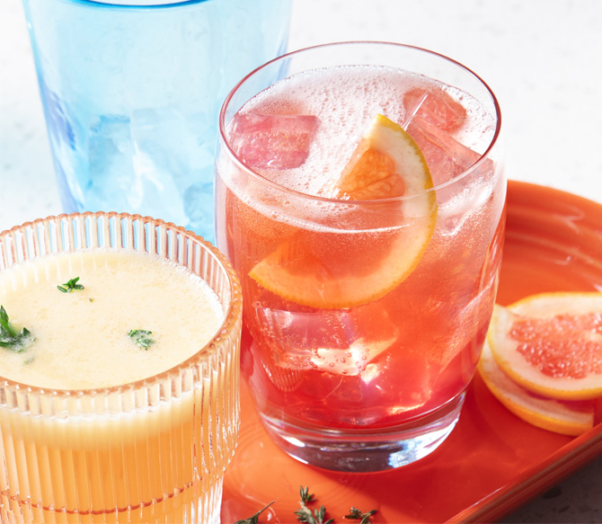  Clear tumbler glass filled with a pink-hued drink made of de-alcoholized beer, Italian soda and cranberry juice, garnished with a slice of pink grapefruit.