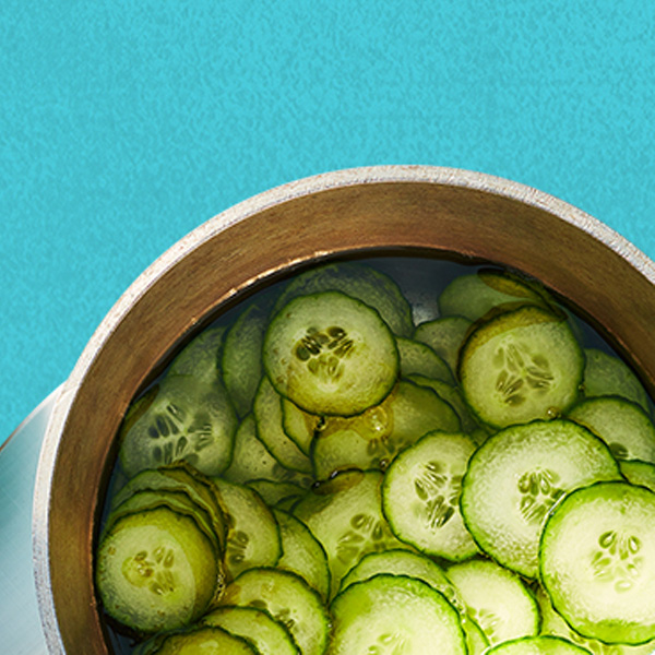 Sliced rounds of pickle in a liquid in a metal pot.