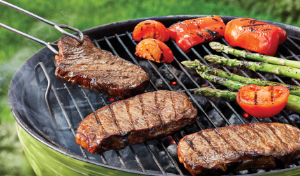 Steaks and vegetables on a green, charcoal grill.