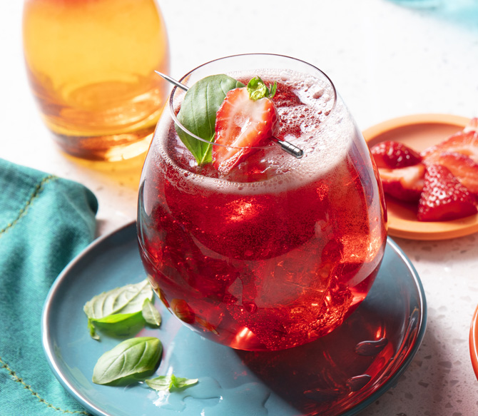 Clear tumbler filled with a lemon iced tea, lemon juice, strawberry soda and basil leaf mocktail, garnished with a strawberry.